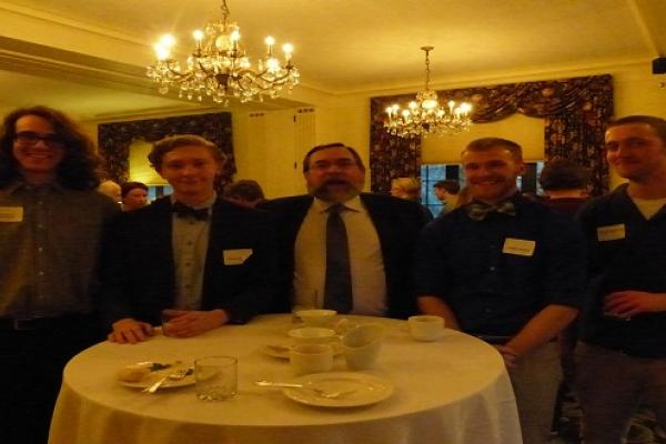 Group of six men standing shoulder to shoulder in a larger room by a table
